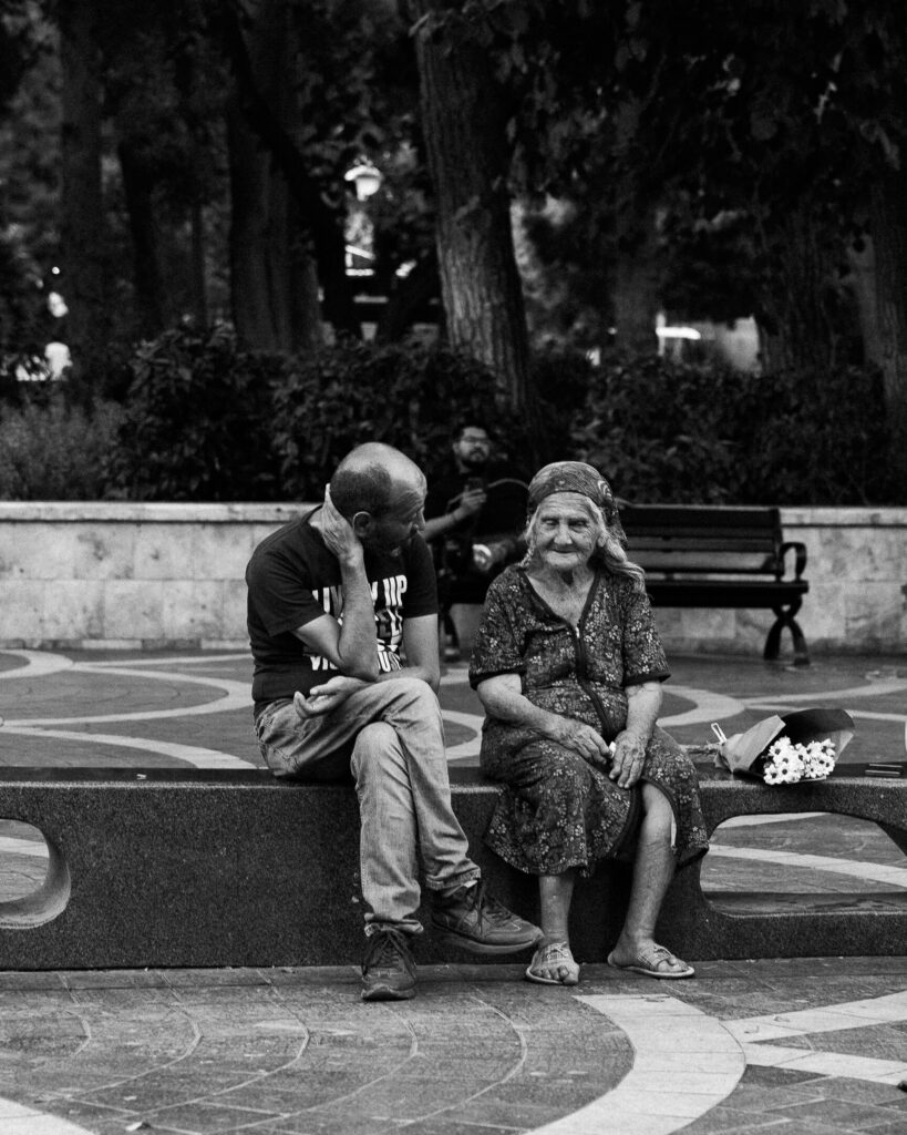 An old couple sitting in a park in Baku with a bouquet of flowers